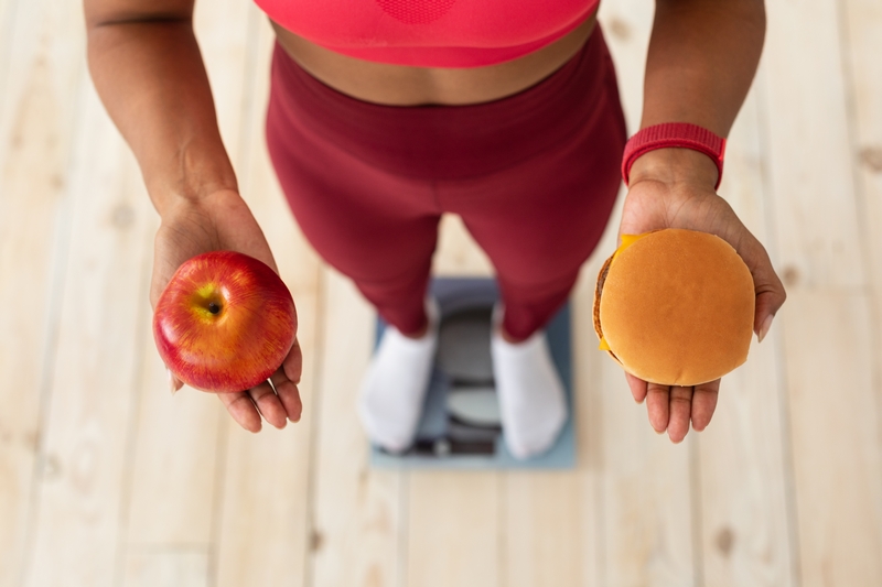 femme sur une balance qui tient un hamburger et une pomme